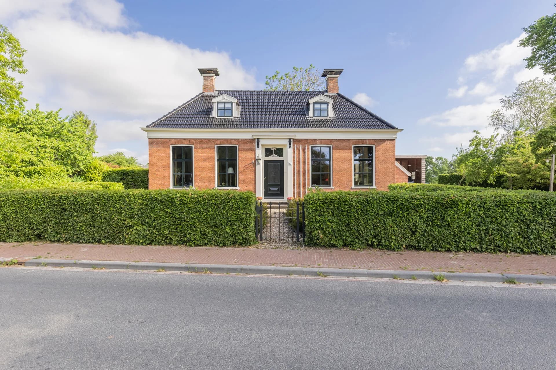 Klassieke pastoriewoning met bakstenen gevel, zwarte ramen en hoge haag, vastgoedfotografie Friesland